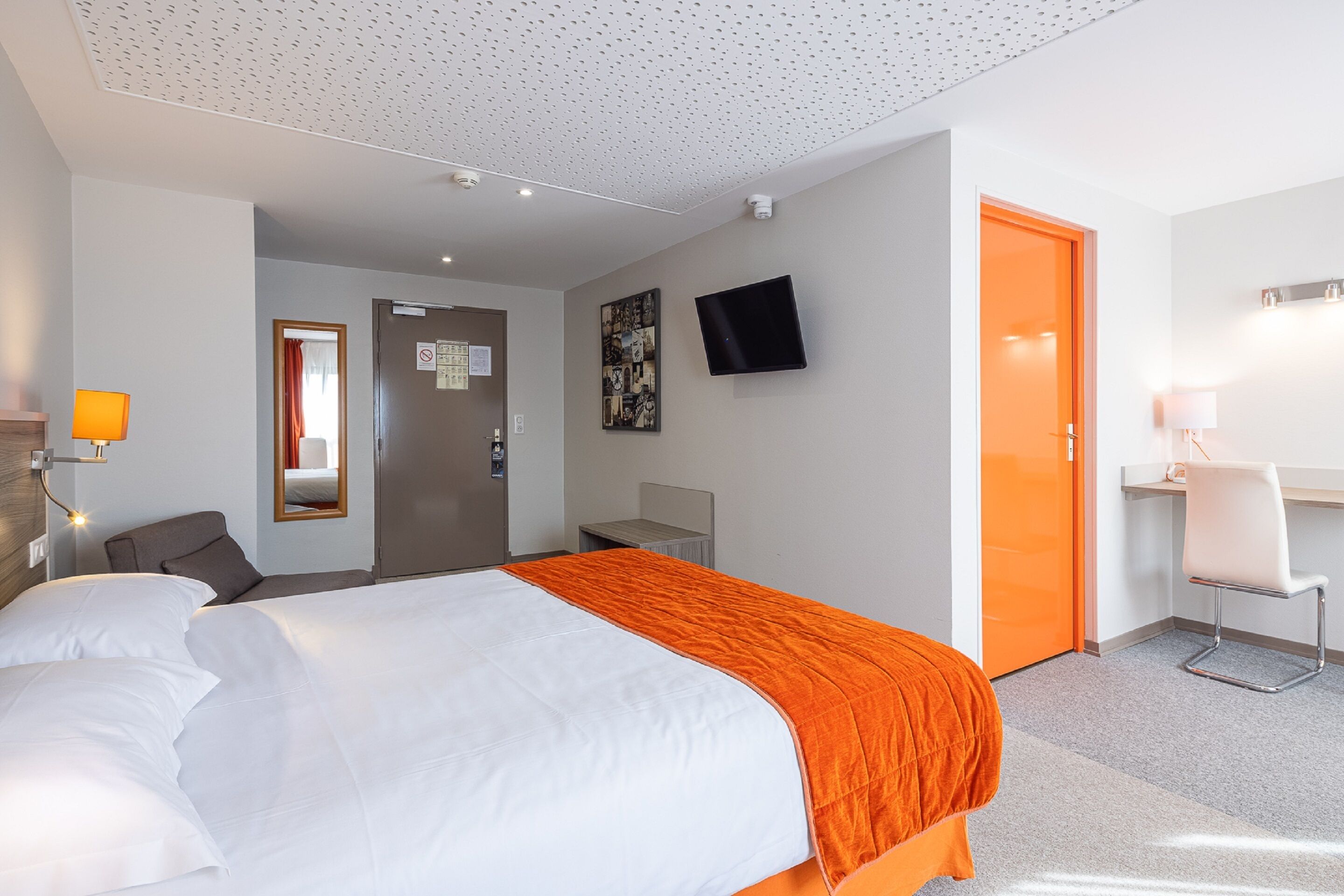 Una habitación de hotel con cama, escritorio, silla, televisión y puerta.