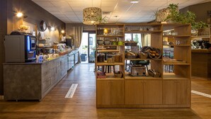 Un coin cuisine avec des meubles en bois, un réfrigérateur et divers appareils de cuisine. On y trouve des étagères remplies d’ustensiles de cuisine et une plante posée sur le dessus.