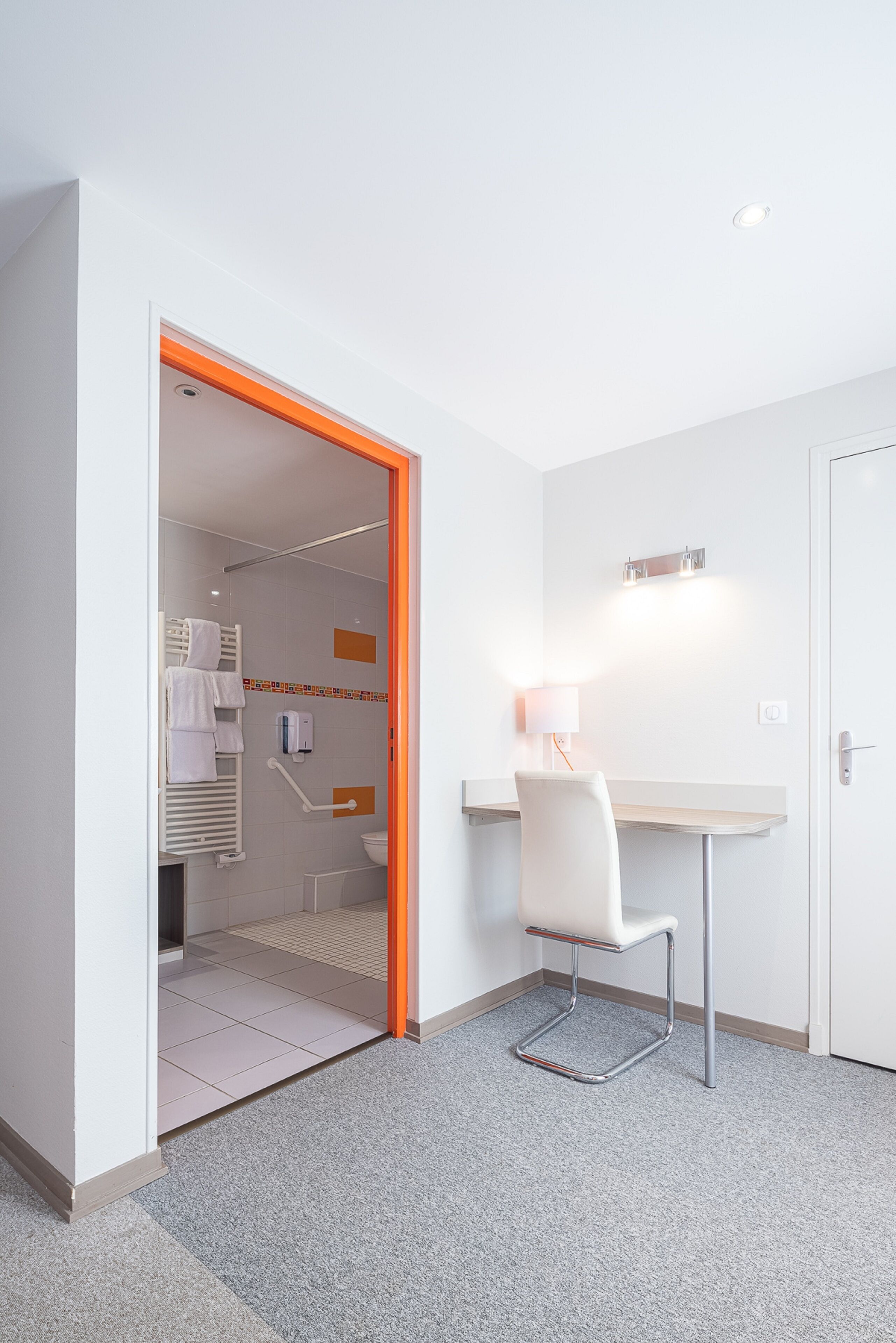 Una habitación de hotel moderna con zona de ducha, un escritorio y una silla, y una puerta.