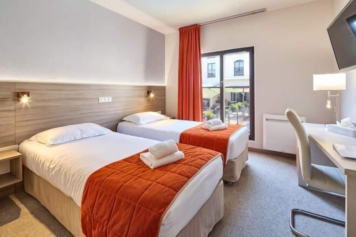 A hotel room with two beds, a desk, a chair, a TV, and a window with a view.