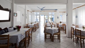 Un espace repas comprenant plusieurs tables et chaises, des murs blancs et de grandes fenêtres.