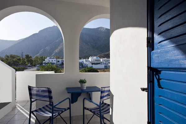 A balcony with two chairs and a table, overlooking a mountainous landscape with white buildings. - Ancient Thera Studios (Santorini)