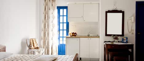 A bedroom with a bed, a chair, a desk, and a small table. There is a window with curtains, a door, and a mirror on the wall.