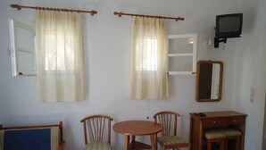 A room with a bed, two chairs, a small table, a TV, and a mirror. - Pension Romantika (Mykonos)