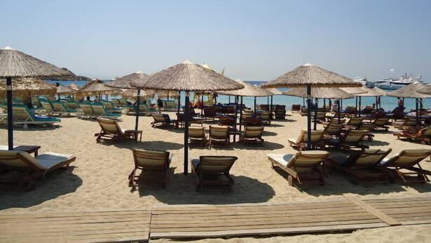 A beach with rows of sun loungers and thatched umbrellas, a wooden deck, and a clear view of the sea. - Pension Romantika (Mykonos)