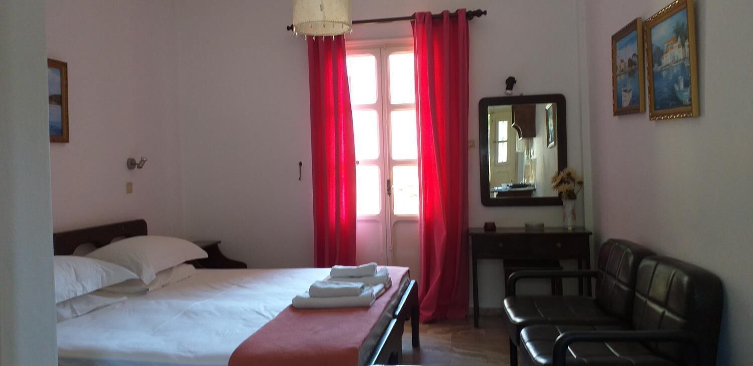 Ein Hotelzimmer mit Bett, Schreibtisch, Stuhl, Spiegel und einem Fenster mit roten Vorhängen.