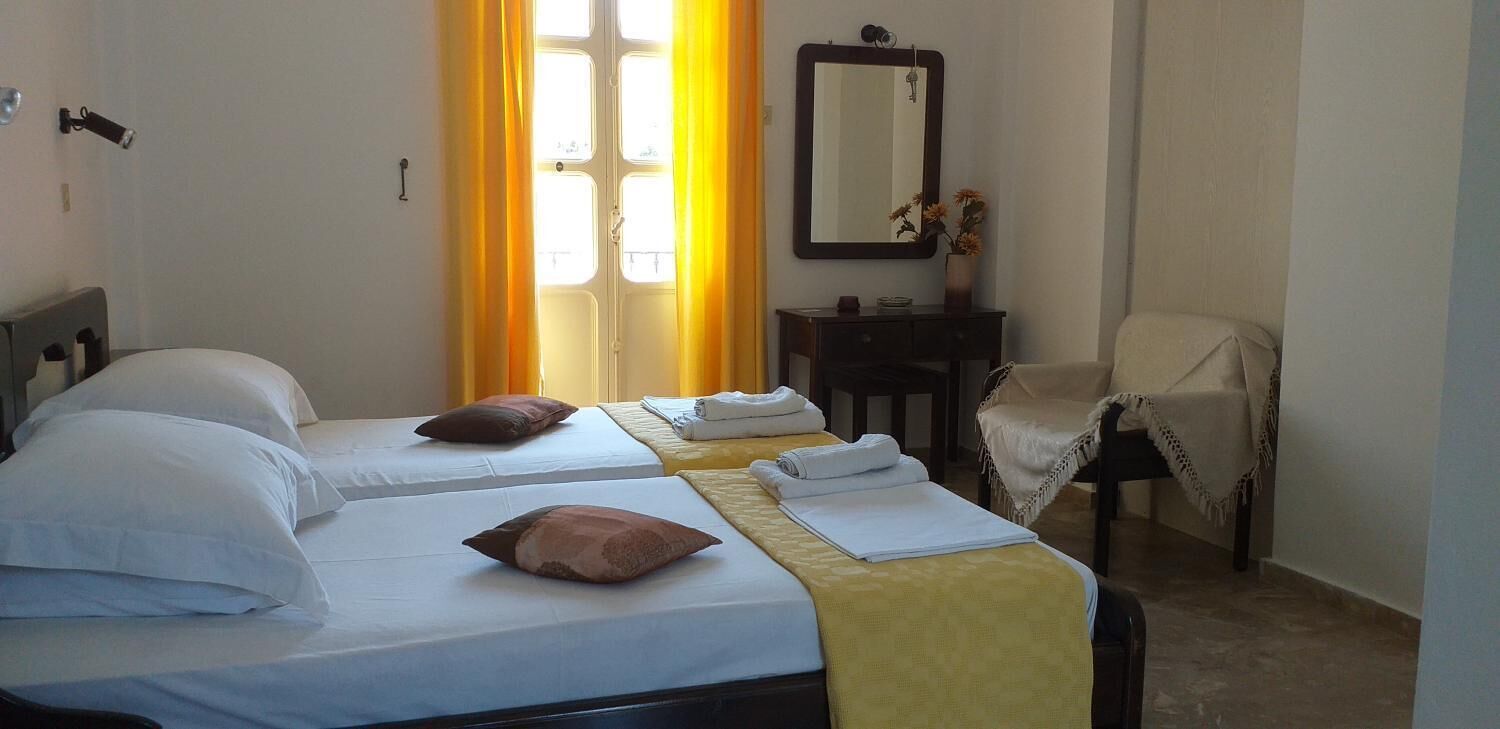 A hotel room with two beds, a small table with a mirror, a chair, and a window with curtains.