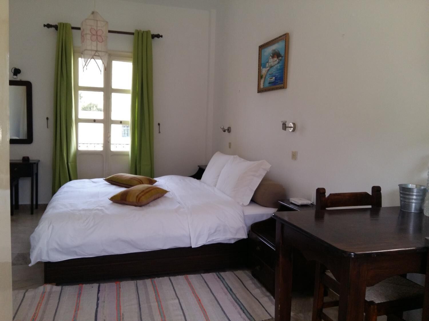 A bedroom with a bed, green curtains, a painting, a desk, and a chair.