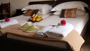 A hotel room with two beds, each with white linens and brown decorative pillows. There is a fruit basket on one bed, a pair of slippers, and a towel on the bed. - Mela Studios (Kalymnos)