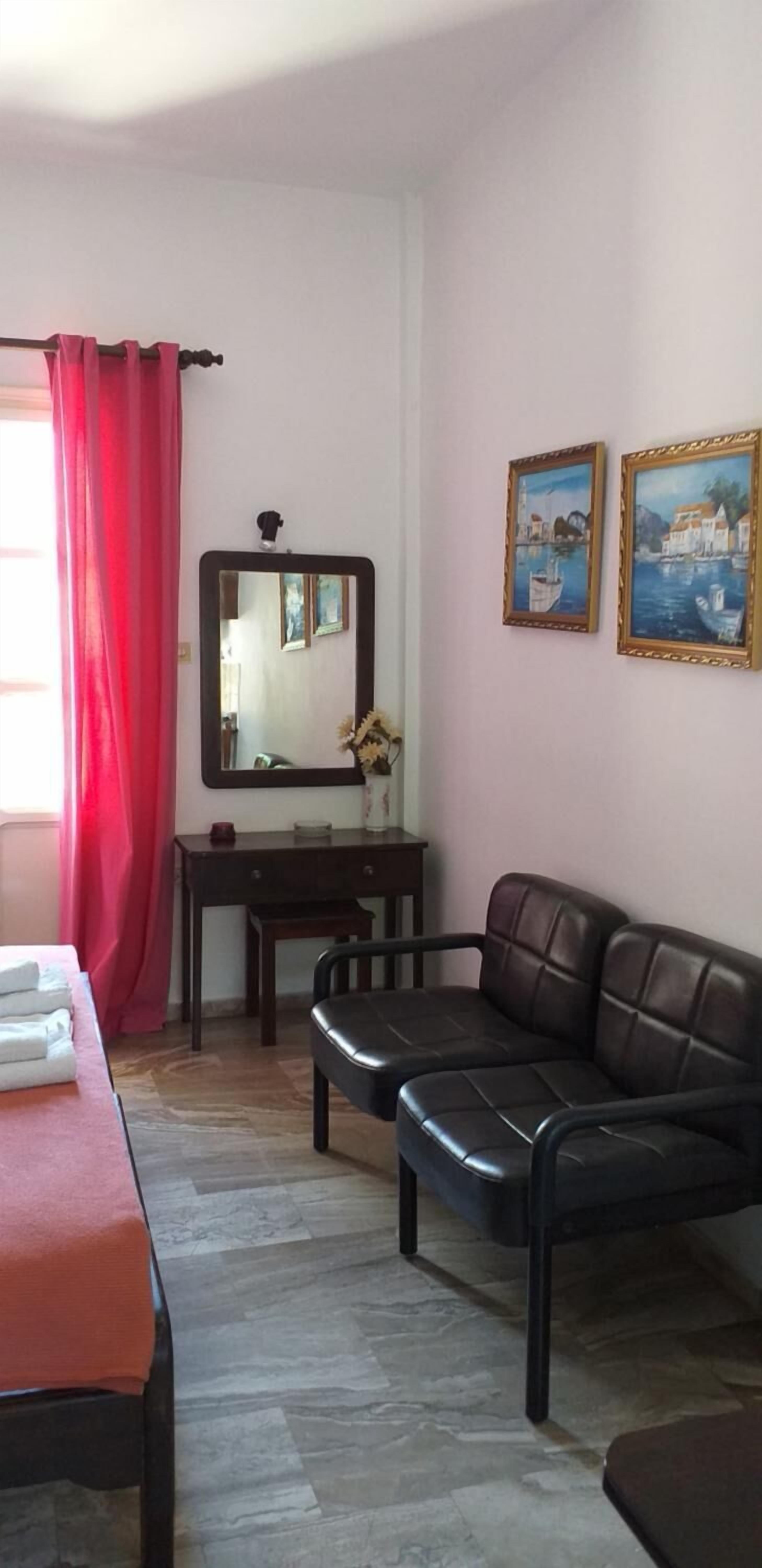 A room with a sofa, a desk, a mirror, and two framed paintings on the wall.