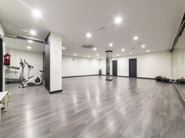 A spacious room with grey wooden flooring, a glass partition, and a row of black doors.