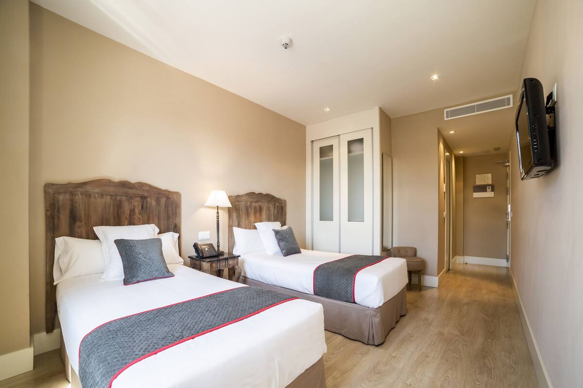 A hotel room with two beds, a desk, a lamp, a TV, and a wardrobe.