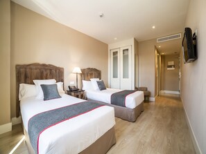 A hotel room with two beds, a desk, a lamp, a TV, and a wardrobe. - Hotel Altora (Tomelloso)