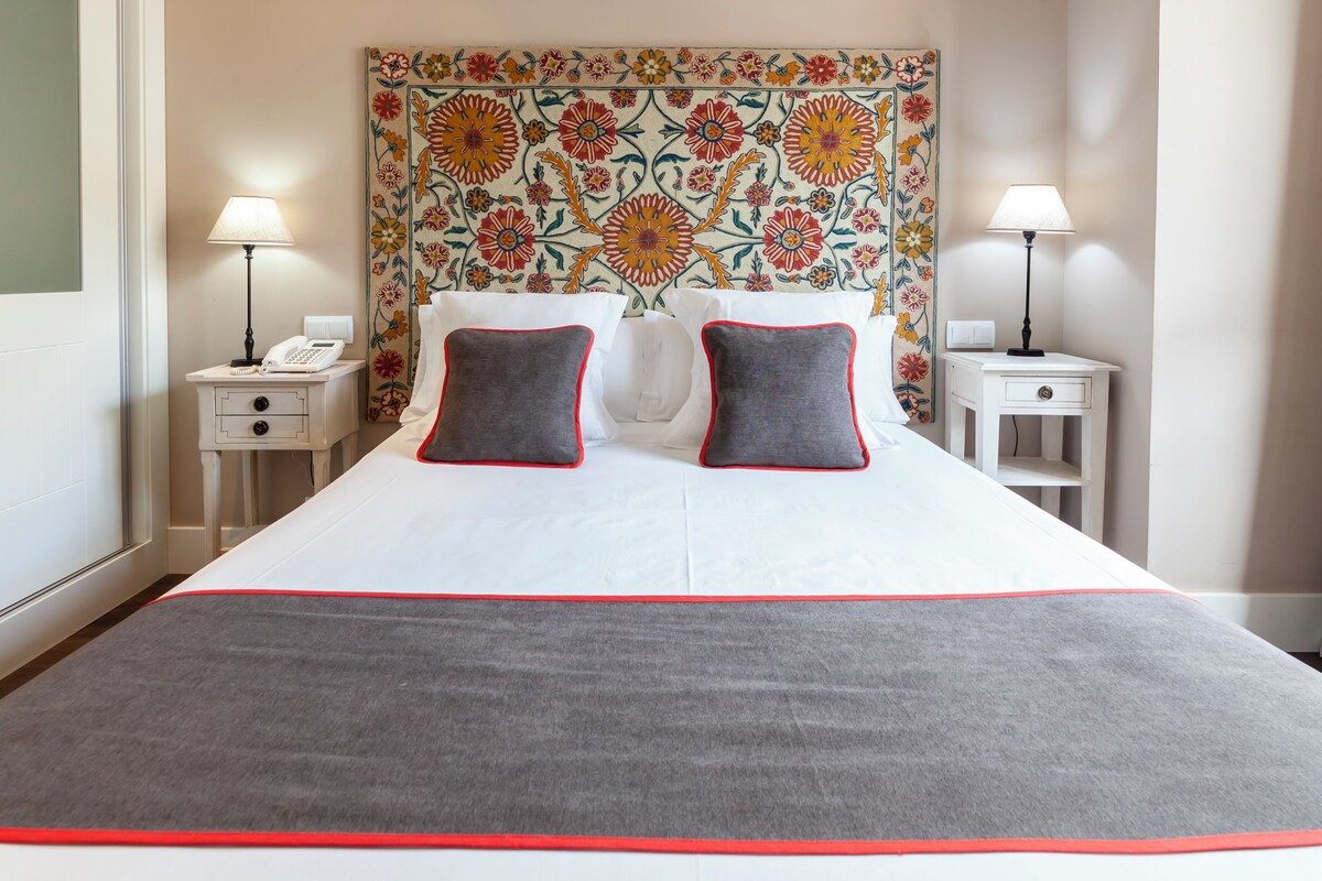 A hotel room with a large bed, two bedside tables, a telephone, and a floral-patterned headboard.