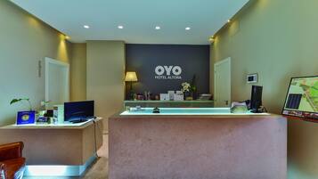 Un mostrador de recepción con un cartel que dice "OYO HOTEL ALTORA" y una pantalla con un mapa.