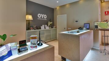 A reception area with a counter, a desk with a computer, a wall-mounted sign for OYO HOTEL ALTORA, a map display, and a fire extinguisher.