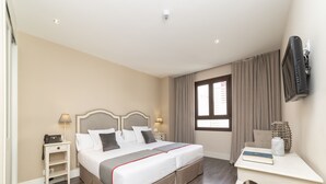 Habitación de hotel con cama doble, mesitas de noche, escritorio, silla, televisor y ventana con cortinas.