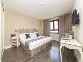 Habitación de hotel con cama doble, mesitas de noche, escritorio, silla, televisor y ventana con cortinas.