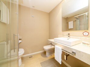 A modern bathroom with a glass shower enclosure, a white toilet, and a sink with a mirror above. - Hotel Altora (Tomelloso)