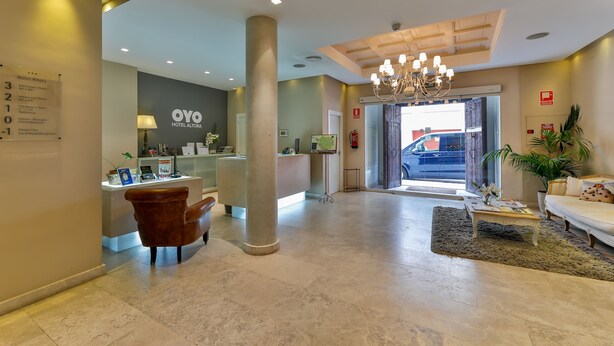 Un vestíbulo de hotel con una recepción, un pilar grande, una araña, un sofá y una mesa de centro.