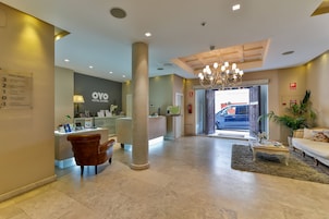 A hotel lobby with a reception desk, a large pillar, a chandelier, a sofa, and a coffee table.