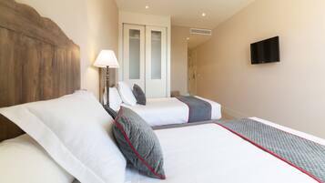 A hotel room with two beds, a wooden headboard, a bedside lamp, a TV, and a door leading to a bathroom.