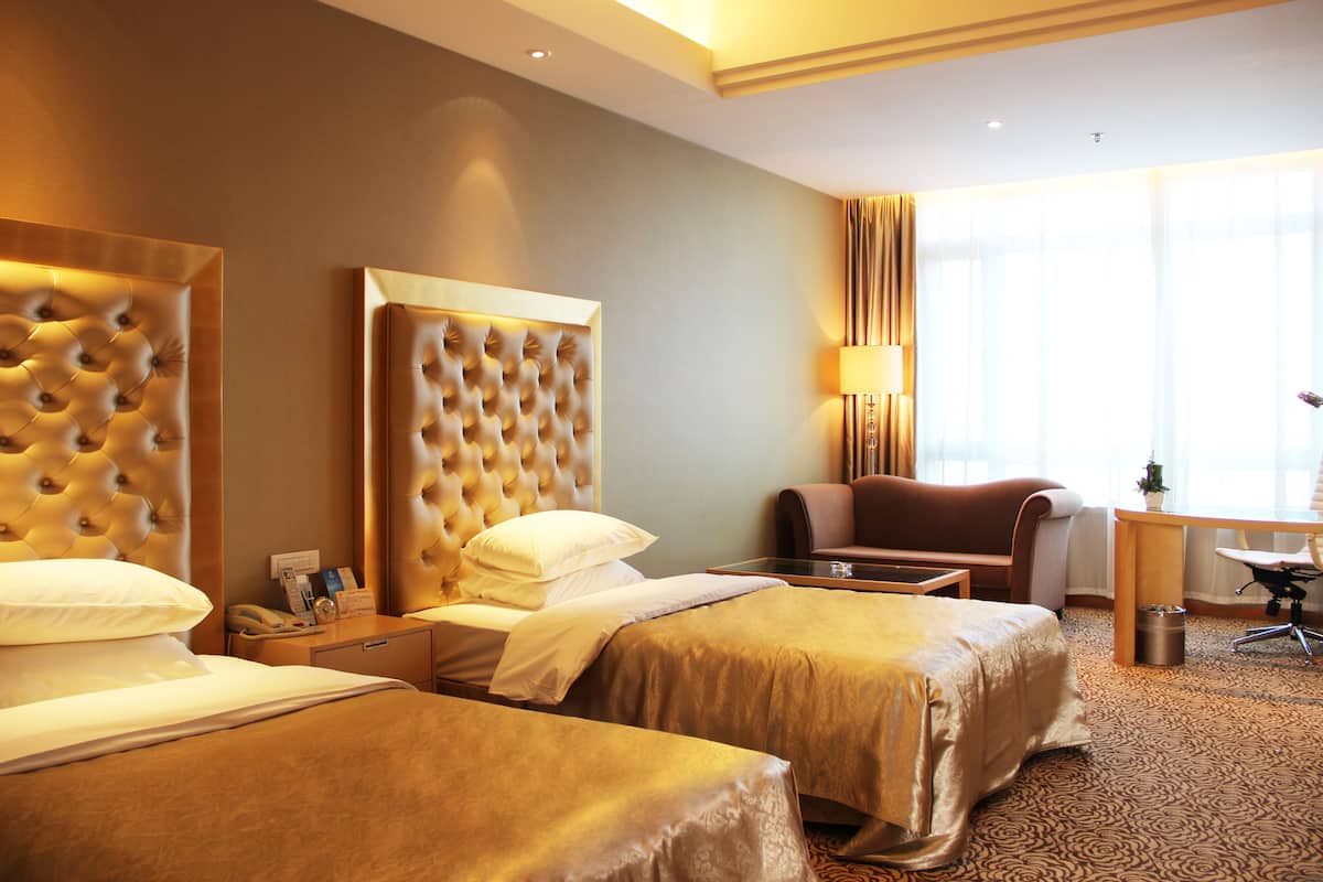 A hotel room with two beds, a desk, a chair, and a large window.