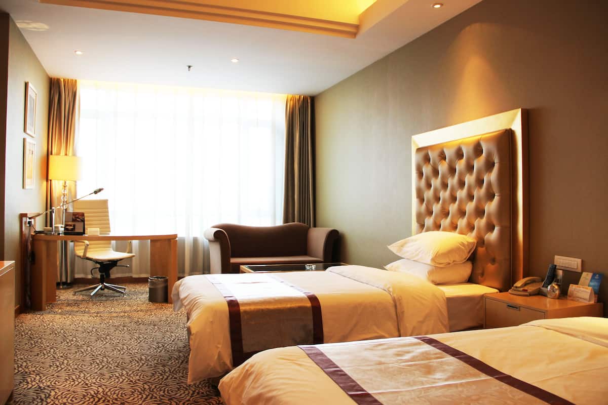 A hotel room with two beds, a desk, a chair, and a large headboard.