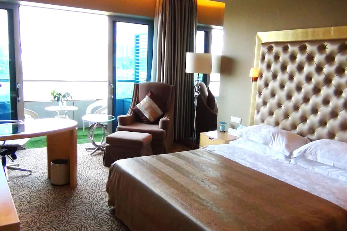 A hotel room with a large bed, a chair, a small table, and a view of the outdoors.