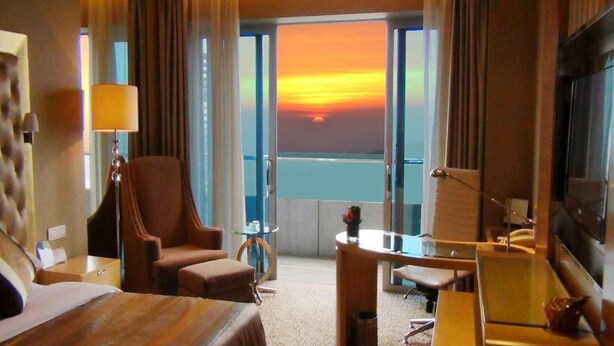 A hotel room with a bed, a desk, a chair, and a view of a sunset over the ocean. - Glarun Jinling Hotel Nanjing (Nanjing)