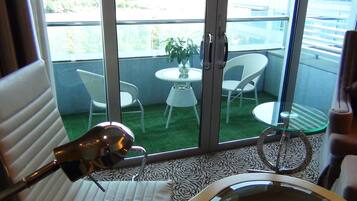 A room with a bed, a chair, a table with a plant, and a balcony with chairs and a table.
