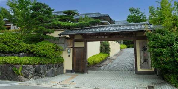 A traditional Japanese gate with a wooden structure and a tiled roof, leading to a pathway.