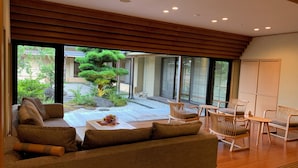 A modern living room with a sofa, chairs, and a coffee table. There is a large window providing a view of a garden and a tree. - Ryotei Rangetsu (Kyoto)