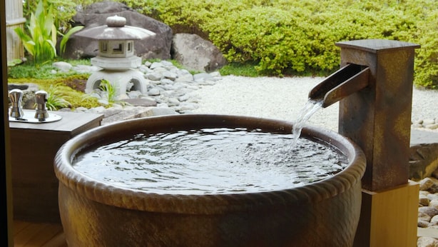 A traditional Japanese hot spring bath with a stone basin and a water spout. - Ryotei Rangetsu (Kyoto)