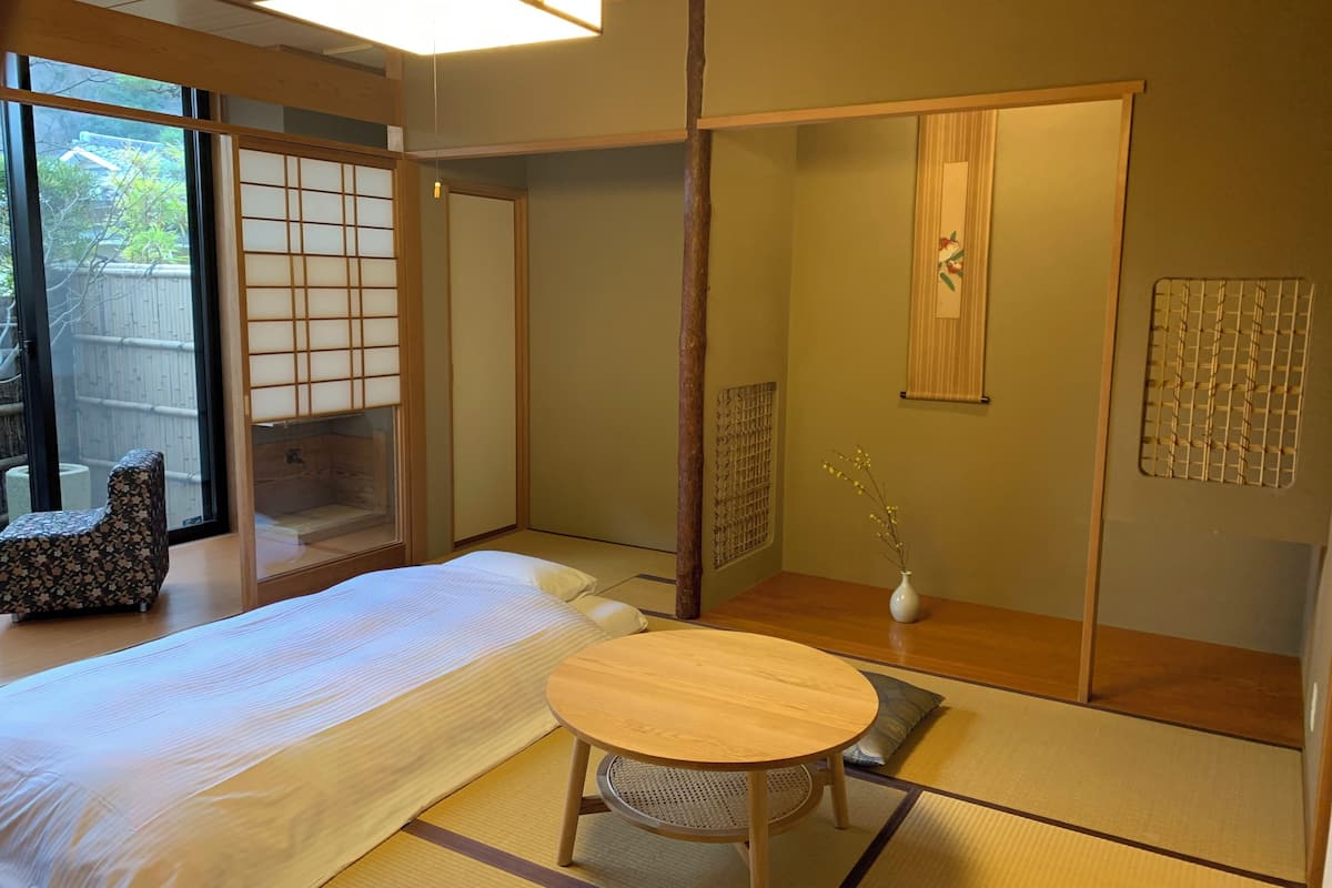 A traditional Japanese room with tatami flooring, a low table, a bed, sliding doors, and a view of the outside.