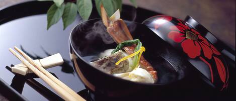 A black bowl with a red floral design, containing food and a pair of chopsticks on a tray.