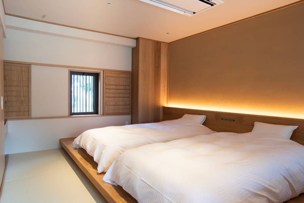 A bedroom with two beds, a window with blinds, and a wooden headboard.