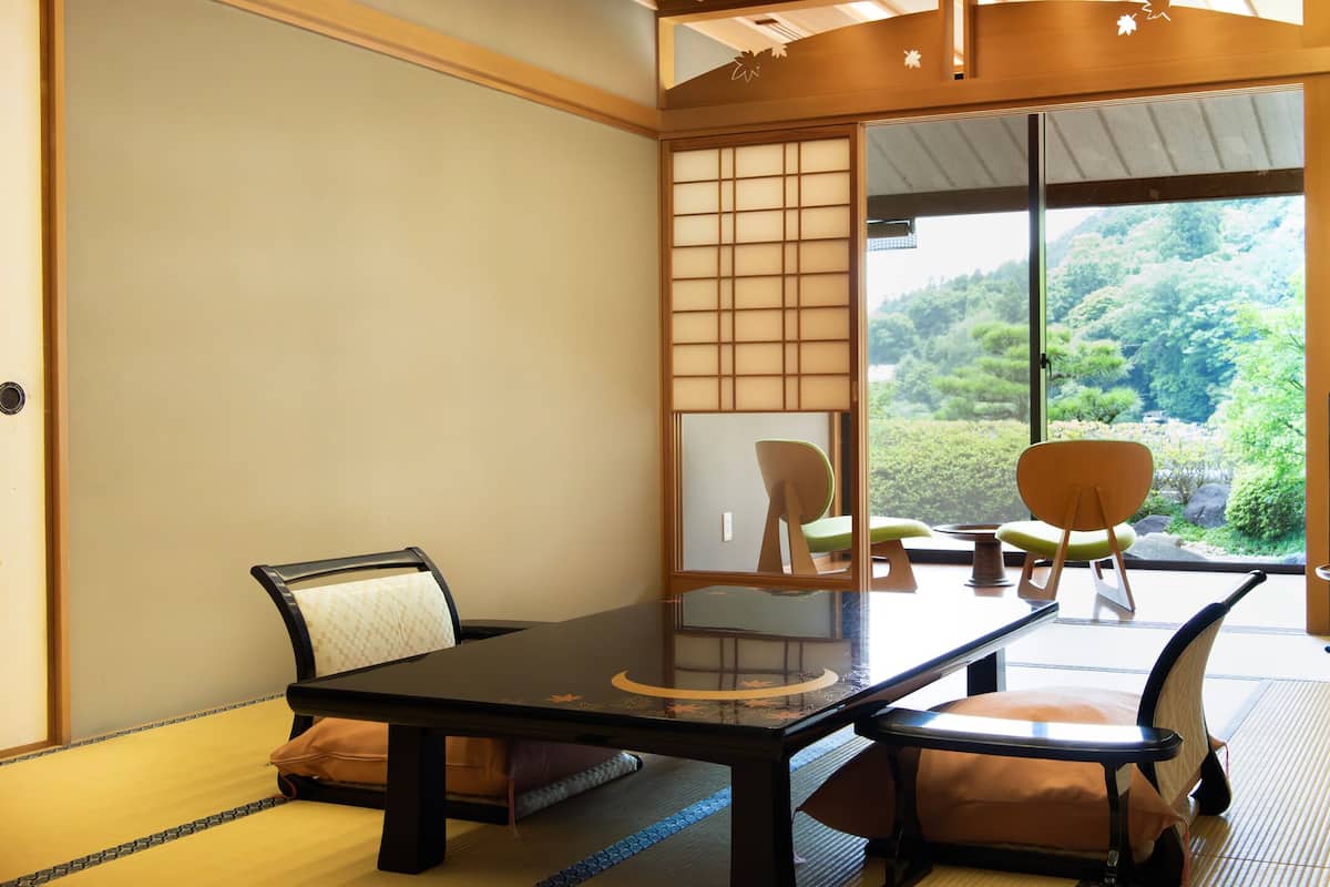 A traditional Japanese room with tatami flooring, a low table, and sliding doors leading to a view of a forested hillside.