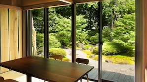 A wooden table and chairs in a room with large windows overlooking a garden with rocks and greenery. - Ryotei Rangetsu (Kyoto)