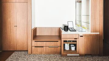 A compact bathroom with a wooden vanity, a sink, and a mirror. There is a small shelf with toiletries and a towel rack above the mirror.
