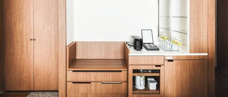 A compact bathroom with a wooden vanity, a sink, and a mirror. There is a small shelf with toiletries and a towel rack above the mirror.