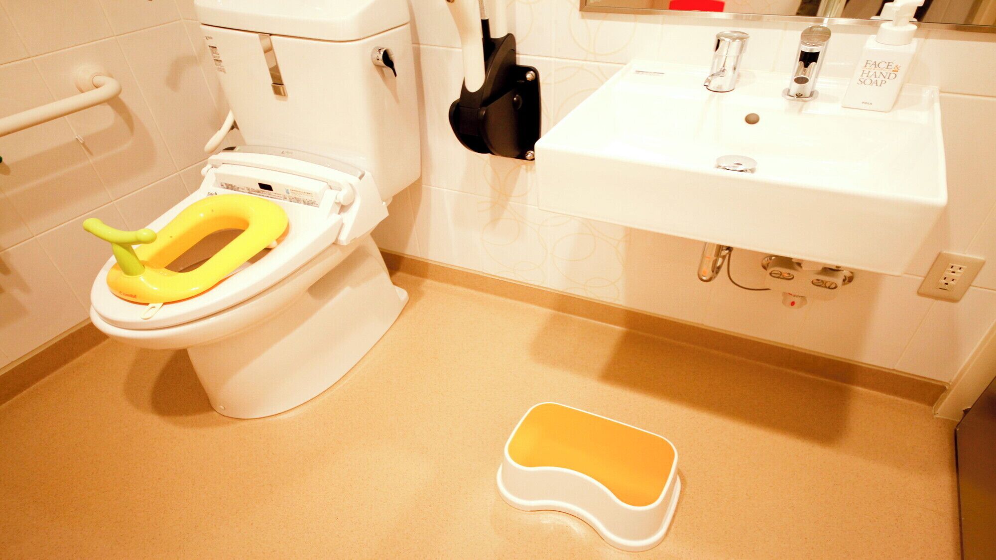 A bathroom with a toilet, sink, and a yellow potty seat.