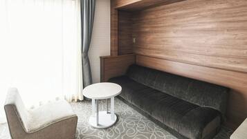 A modern hotel room with a grey sofa, a small round table, and a wooden accent wall.