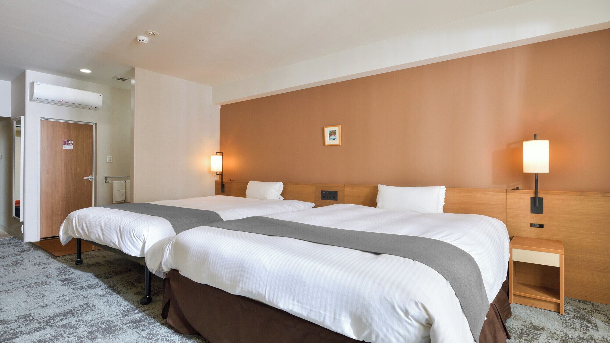Una habitación de hotel con dos camas, cabecero de madera, un cuadro colgado en la pared y lámparas de noche.