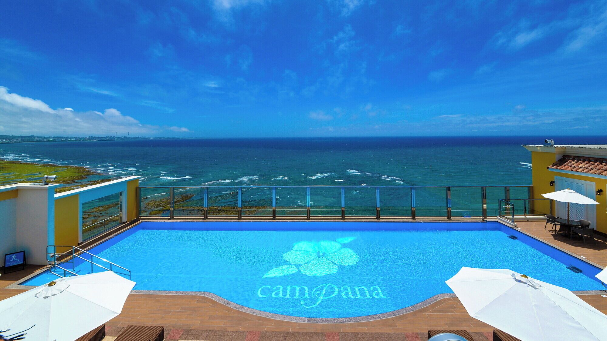 Una piscina con el logotipo 'campana', vistas al océano y un patio con sombrillas.
