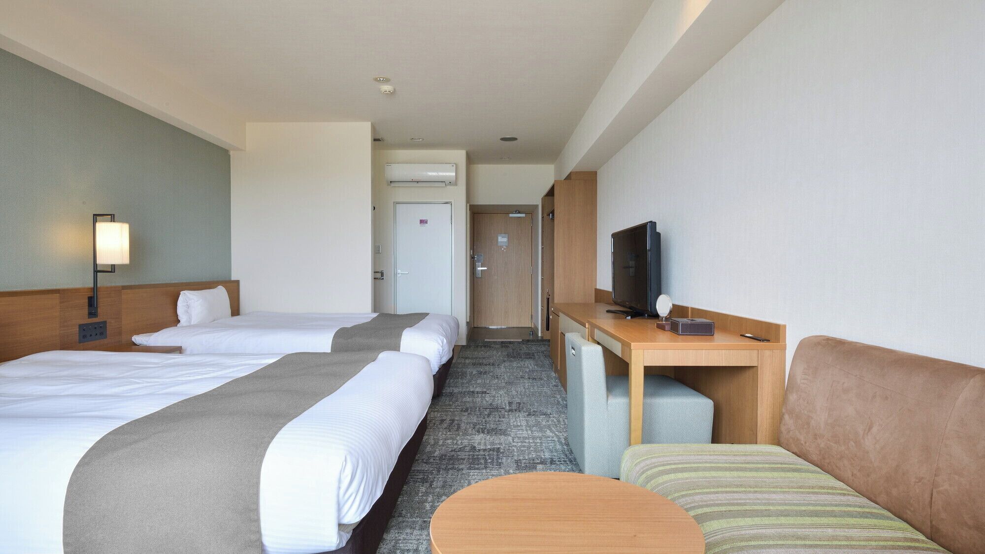 A hotel room with two beds, a desk with a TV, a sofa, and a lamp.