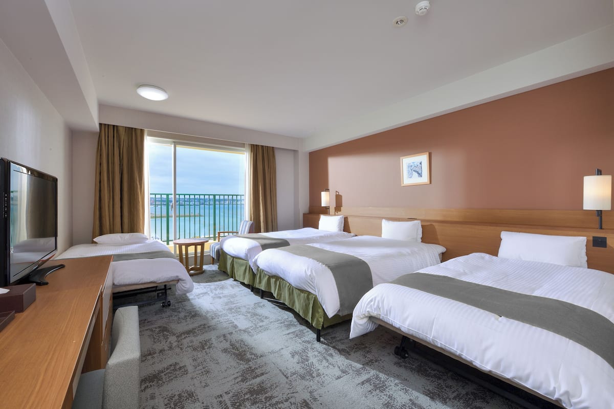 Une chambre d’hôtel avec trois lits, un bureau, une télévision et un balcon avec vue.