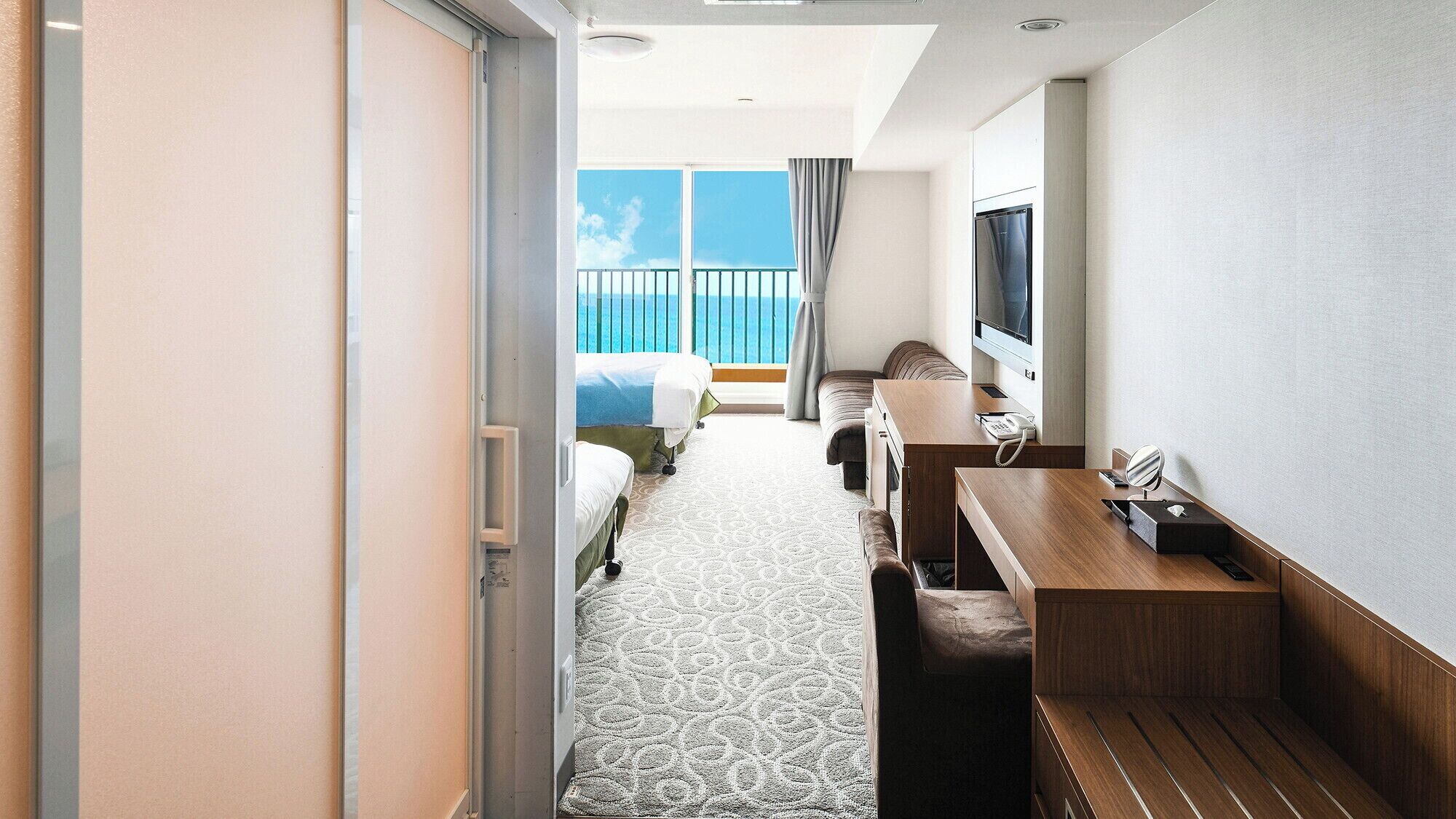Habitación de hotel con cama, escritorio, silla, televisión y balcón con vista al mar.
