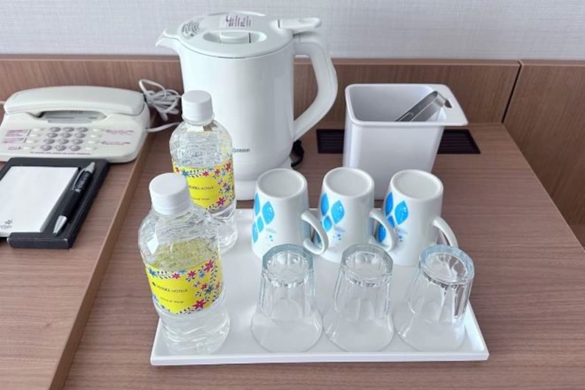 A tray with a kettle, cups, and bottles on a wooden table.