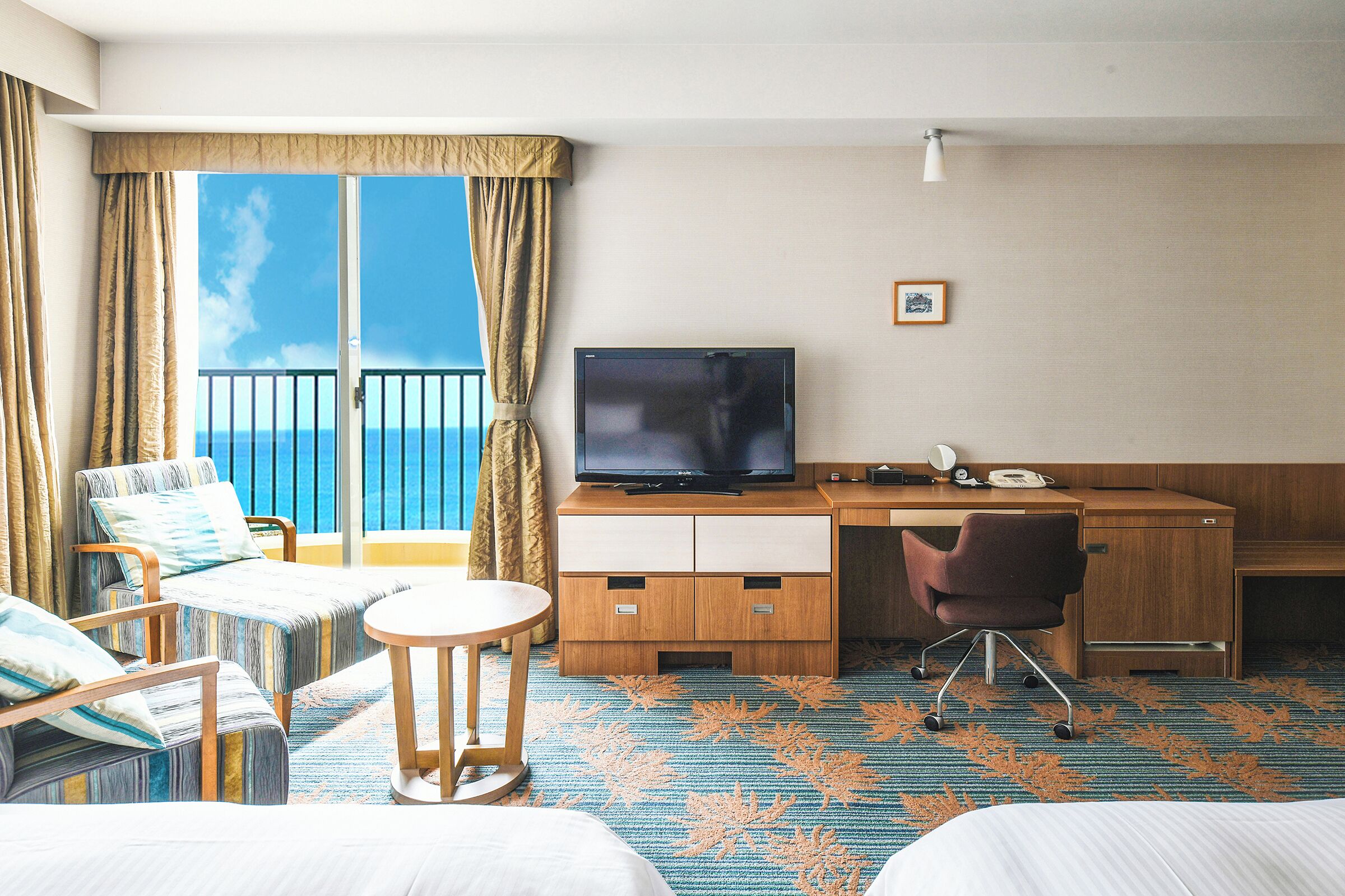 Una habitación de hotel con balcón, televisión, escritorio y una silla.